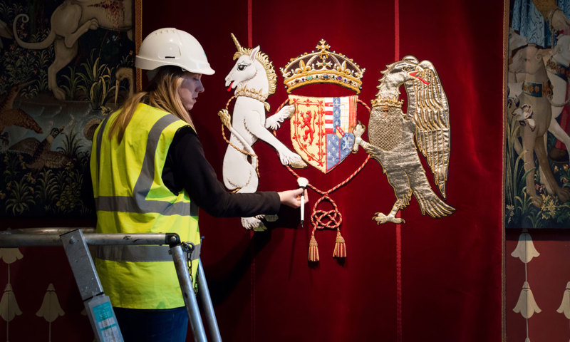 A woman in a yellow high visibility jacket on a ladder cleaning the rope of an embroidered emblem