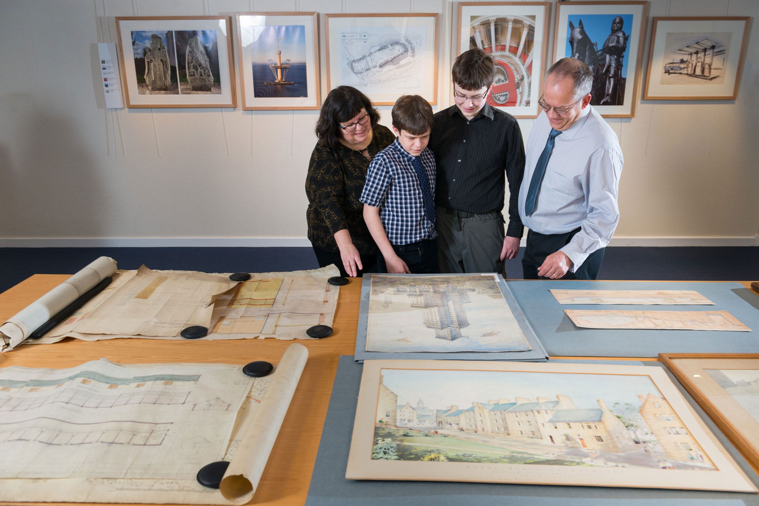 A photograph of a family looking at drawings and paintings of architecture laid out on a table
