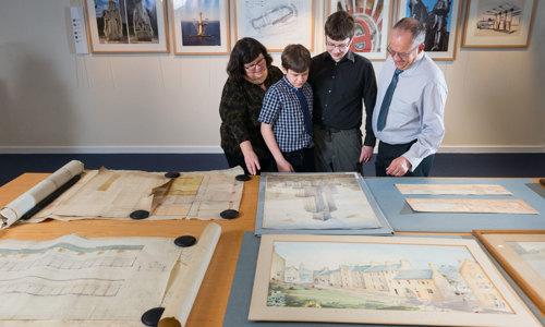 A photograph of a family looking at drawings and paintings of architecture laid out on a table