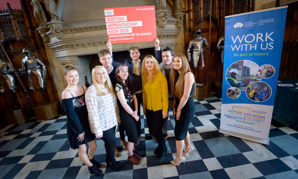 8 young people smile for the camera in front of a sign advertising Scottish Apprenticeship Week 2018