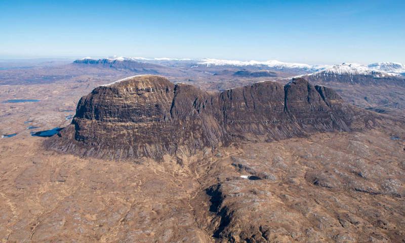 A photograph of a mountain from the air with blue skies above.