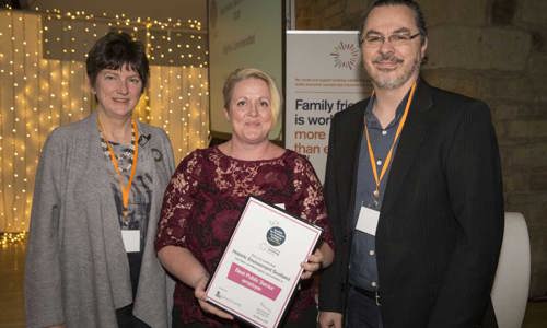 A photograph of two women and a man smiling at the camera holding a large certificate