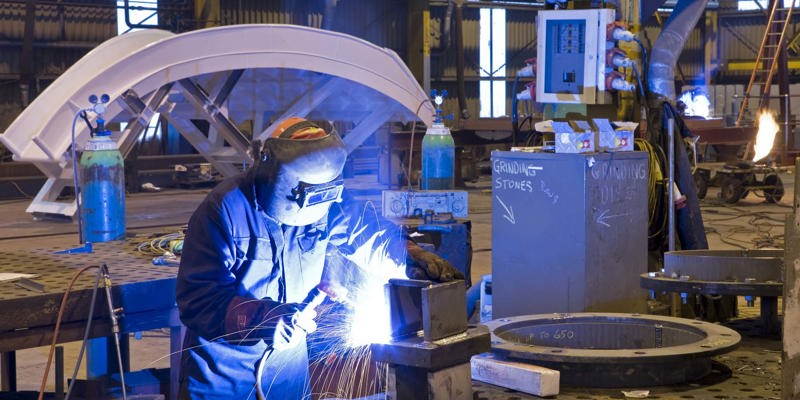 A welder wearing safety equipment welds a piece of metal in an industrial environment 