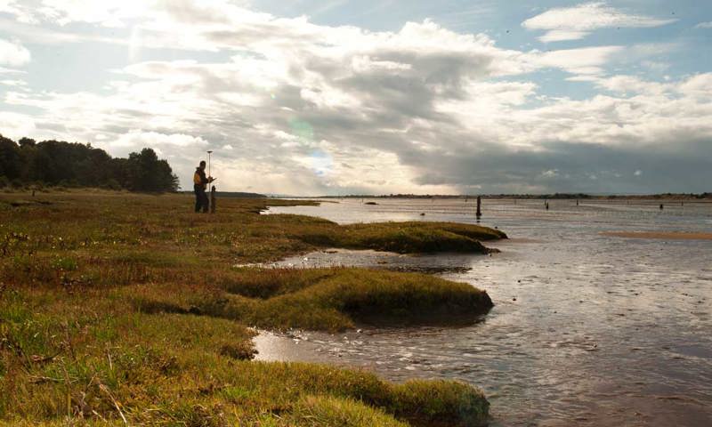 A man with a clipboard looks out over a body of water.