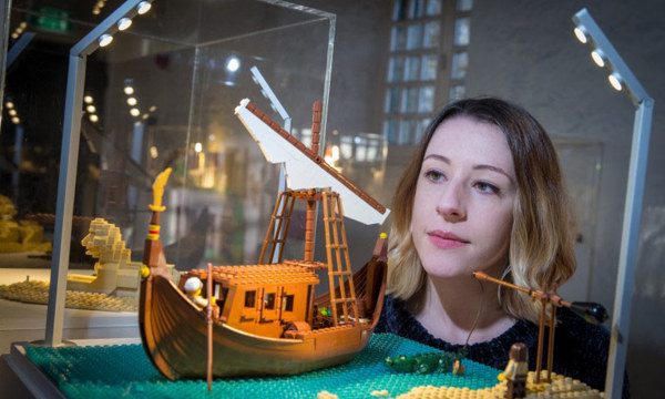 A woman looks into a glass cabinet with a lego display of a ship on the ocean 