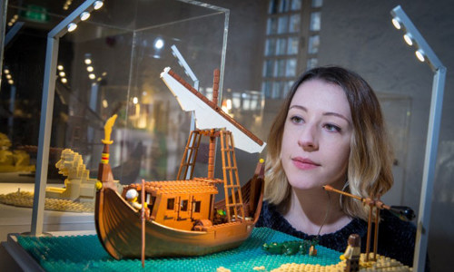 A woman looks into a glass cabinet with a lego display of a ship on the ocean 