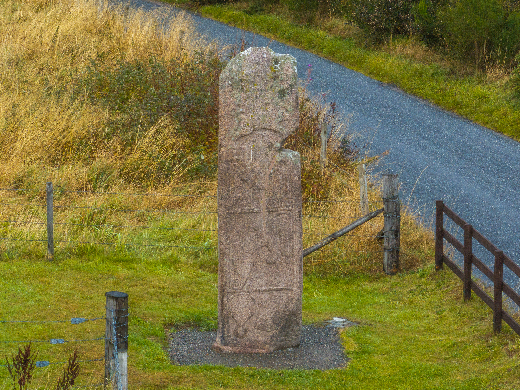 Close view of the Maiden Stone from an elevated angle, showing its carved patterns and surrounding grassland.