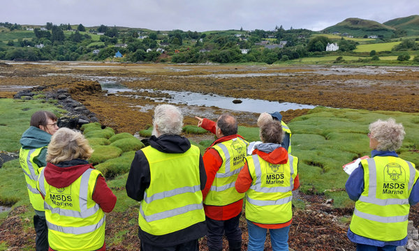 A group of people wearing safety jackets with MSDS Marine text and logo on the back, looking out over an island