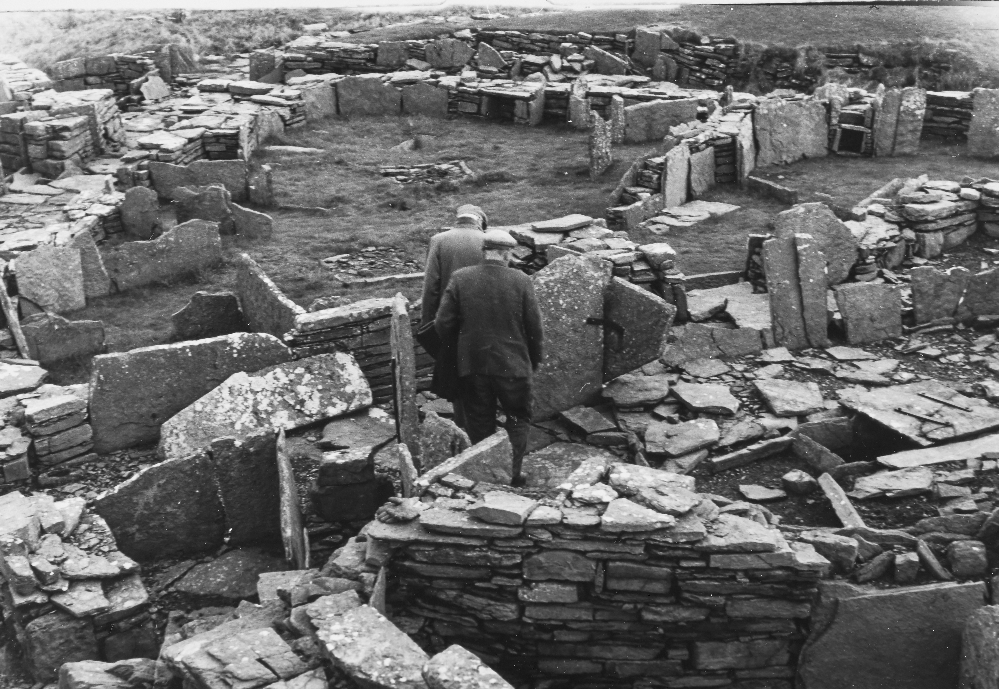 Two men walk between slabs, some seeming to be scattered and others in the shapes of walls