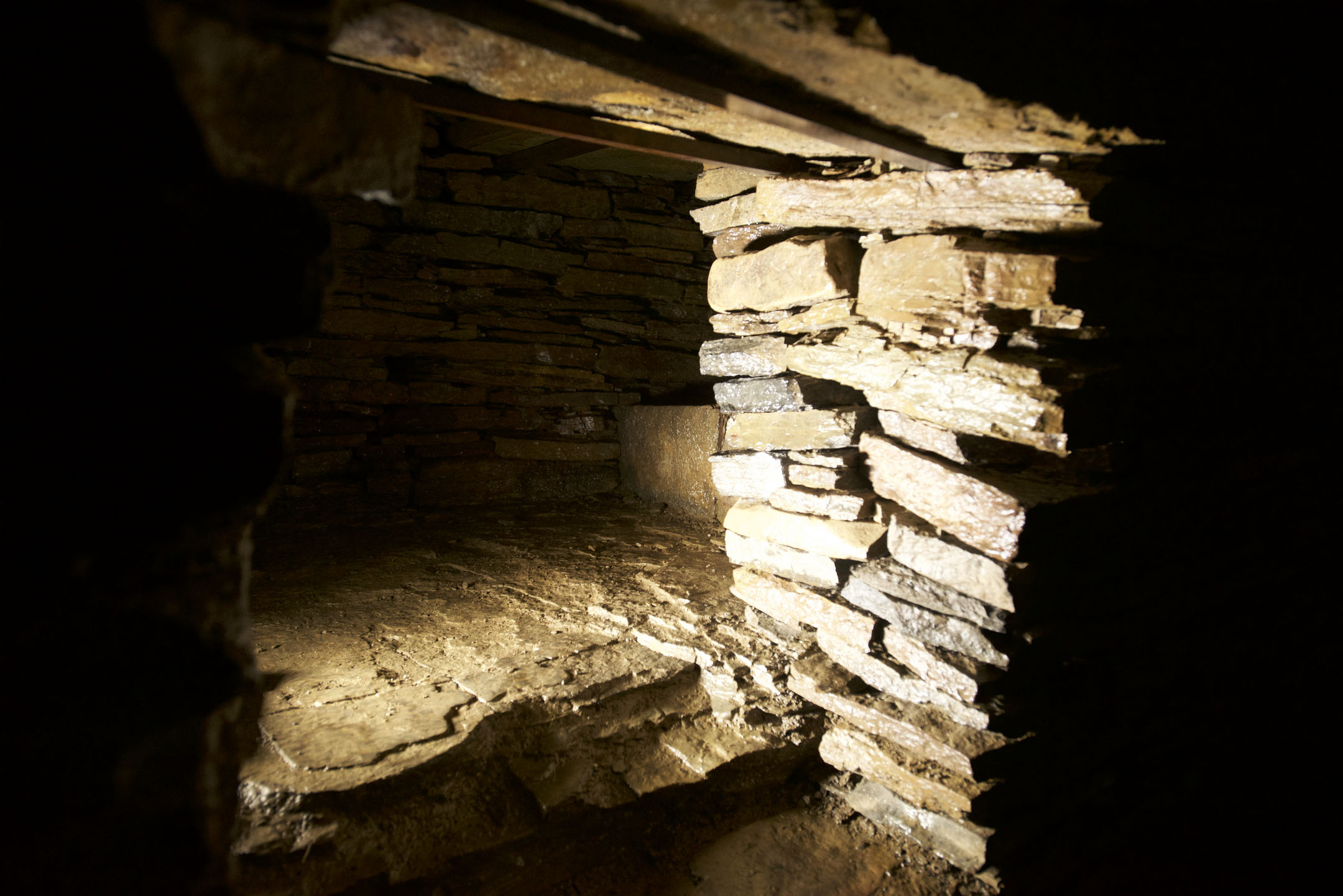 Small side cell within stone chamber, stacked flagstones lit by a beam of light.