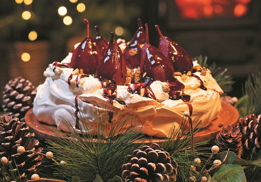 A perfectly cooked pavlova, topped with halved pears that have been poached in wine and remaining syrup poured over along with crushed pistachios 
