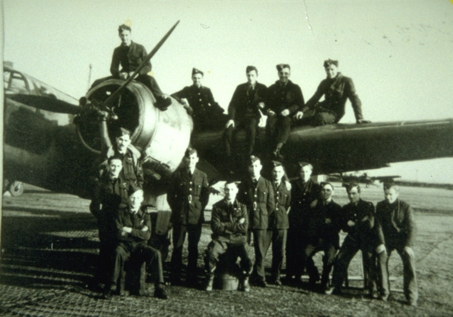 A black and white photograph of an airforce squadron posed in front of their bomber plane.