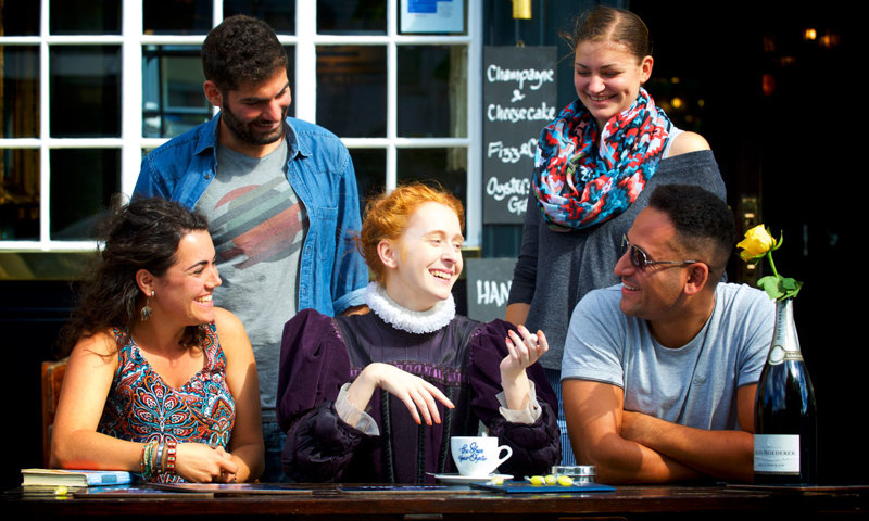 A group of people dressed in modern clothes gathered around a woman with red hair in a historic purple dress.
