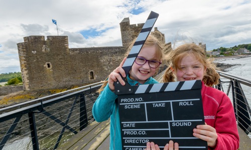 two young girls with a film clapperboard stand in front of Blackness Castle