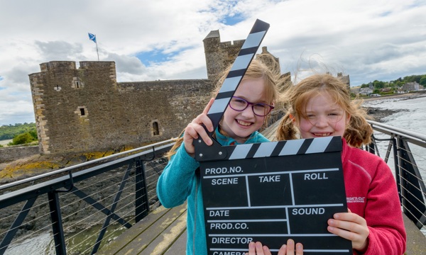two young girls with a film clapperboard stand in front of Blackness Castle