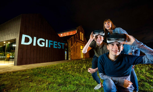 Two teenagers and adult kneel outside the Engine Shed in Stirling wearing VR headsets