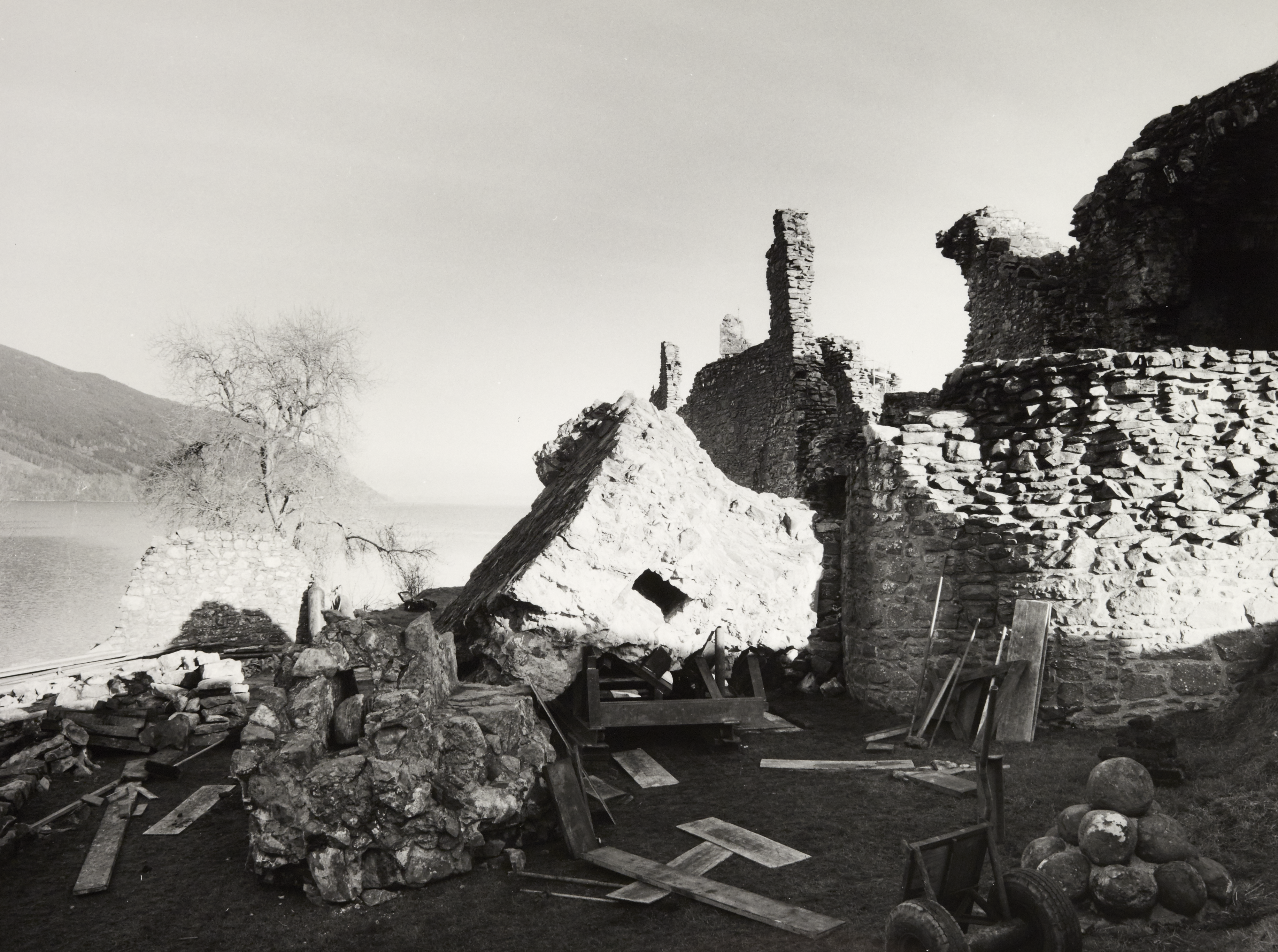 Black and white photo of castle ruin with equipment and planks strewn around due to ongoing work