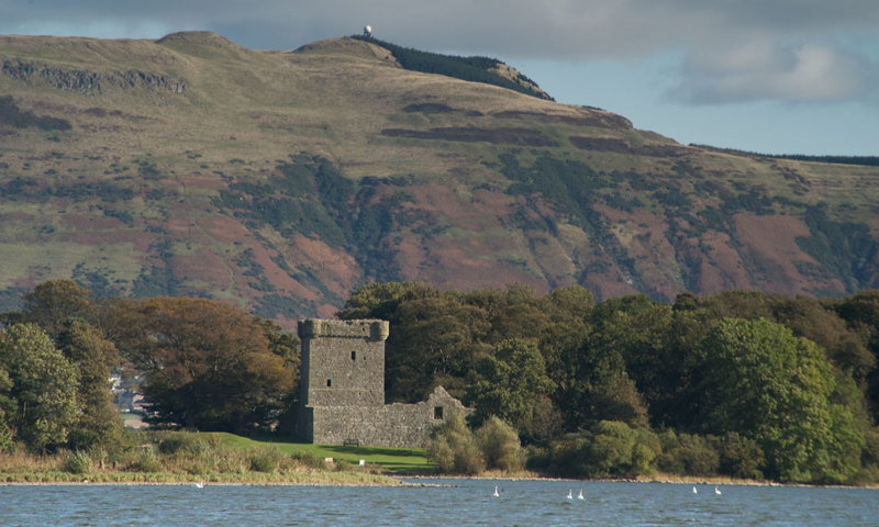 A castle by water in front of a hill.