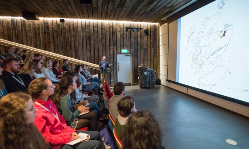 A group of people sitting in the auditorium at the Engine Shed looking at a large screen which has a map of Scotland on it