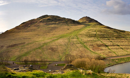 A large hill covered in grass with a small lake nearby.