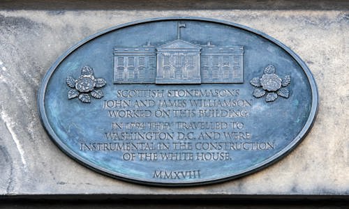 A detailed photo of a commemorative plaque reading "Scottish stonemasons John and James Williamson worked on this building. In 1794 they travelled to Washington D.C. and were instrumental in the construction of The White House." 