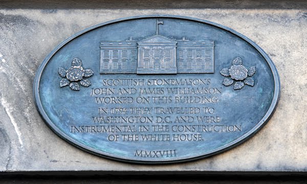 A detailed photo of a commemorative plaque reading "Scottish stonemasons John and James Williamson worked on this building. In 1794 they travelled to Washington D.C. and were instrumental in the construction of The White House." 