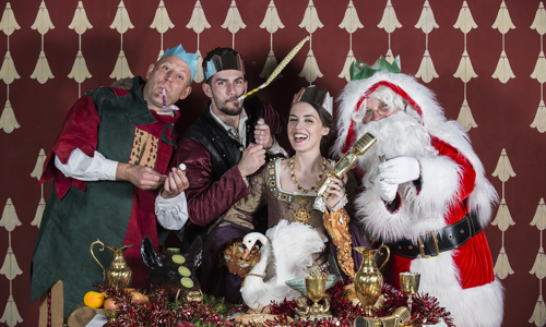 A merry group of people in medieval dress celebrate with Santa