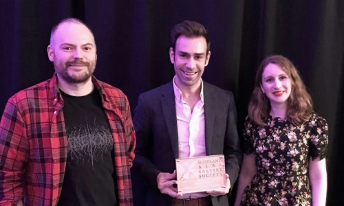 Three winners stand holding their commendation award against a black curtain