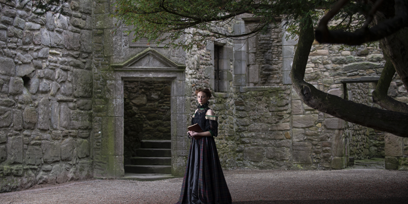 A woman in a Mary Queen of Scots inspired dress stands in the courtyard at Craigmillar Castle