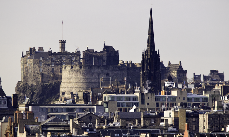 Edinburgh Castle can be seen dominating the city skyline across the rooftops.  