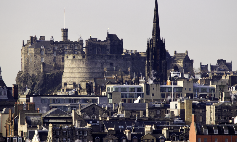 Edinburgh Castle can be seen dominating the city skyline across the rooftops.  