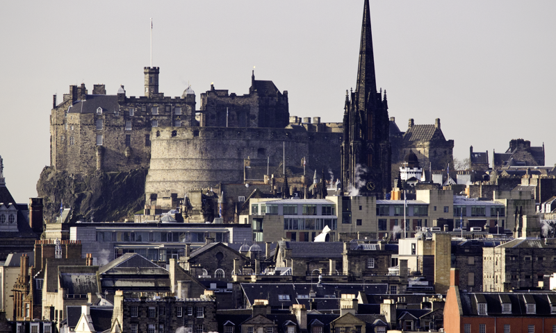 Edinburgh Castle can be seen dominating the city skyline across the rooftops.