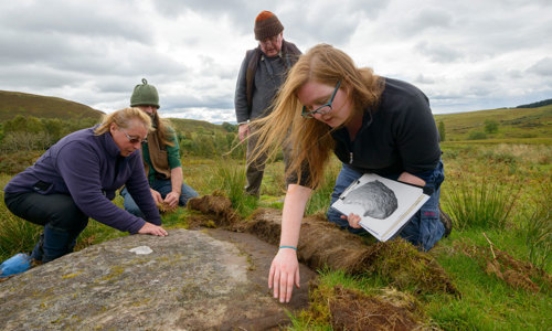A group of people investigate local rock art.