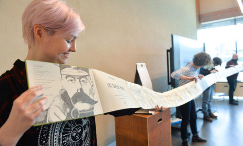 A community group working on a project together hold up a long fold-out book.