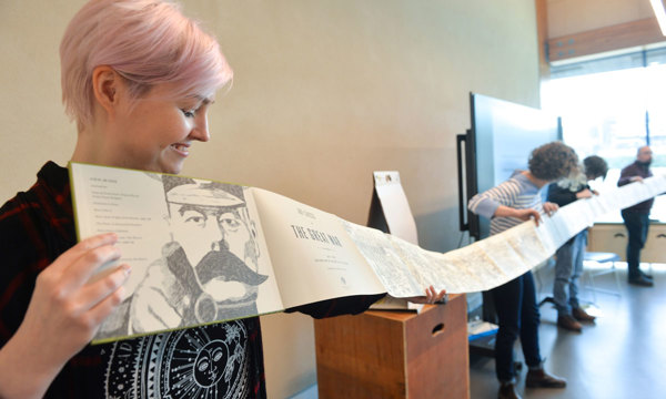 A community group working on a project together hold up a long fold-out book.