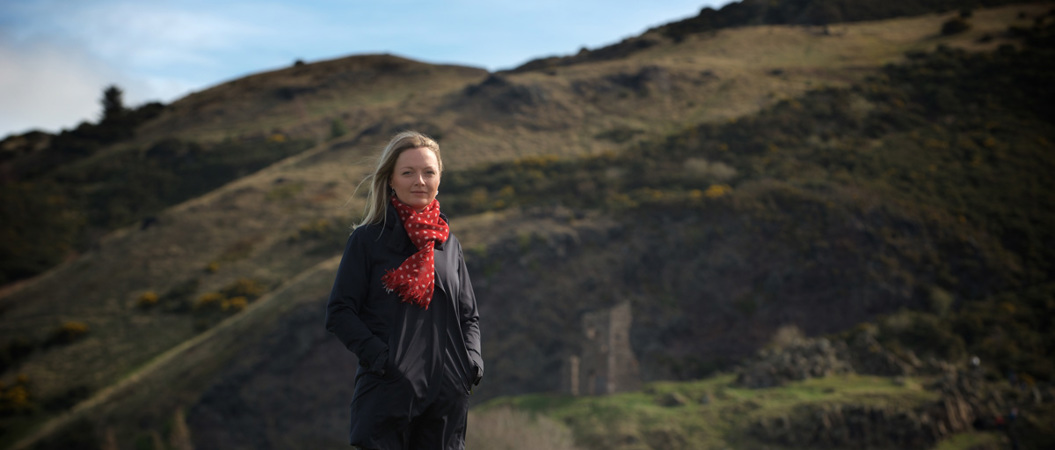 A woman with blonde hair and red scarf standing in a park.