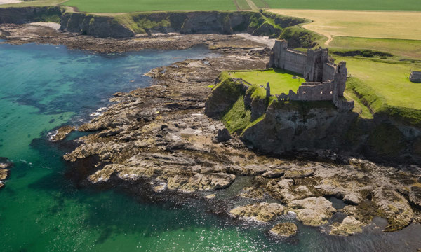 A castle on the side of a cliff beside turquoise sea.