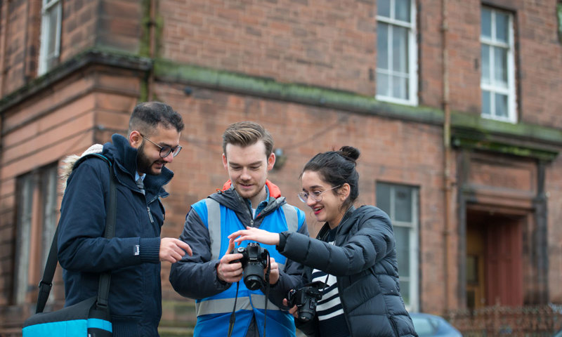 Three project participants review a photograph on a digital camera.
