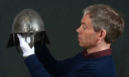 A person wearing white gloves holding up a historic metal helmet