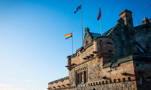 The gateway to a castle on a sunny day with three flags flying above the entrance.