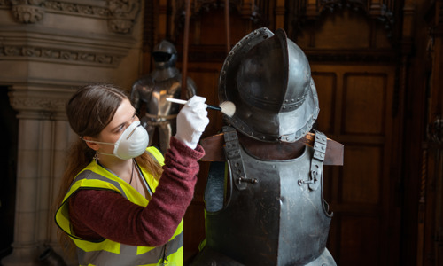 A conservation apprentice works on a set of armour with a fine brush.