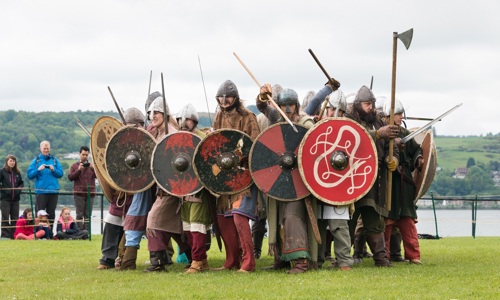 A group of reenactors dressed as Vikings brandish weapons and shields