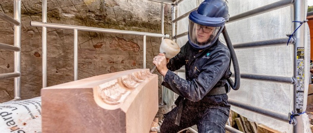 A stonemason carves into a large piece of red stone