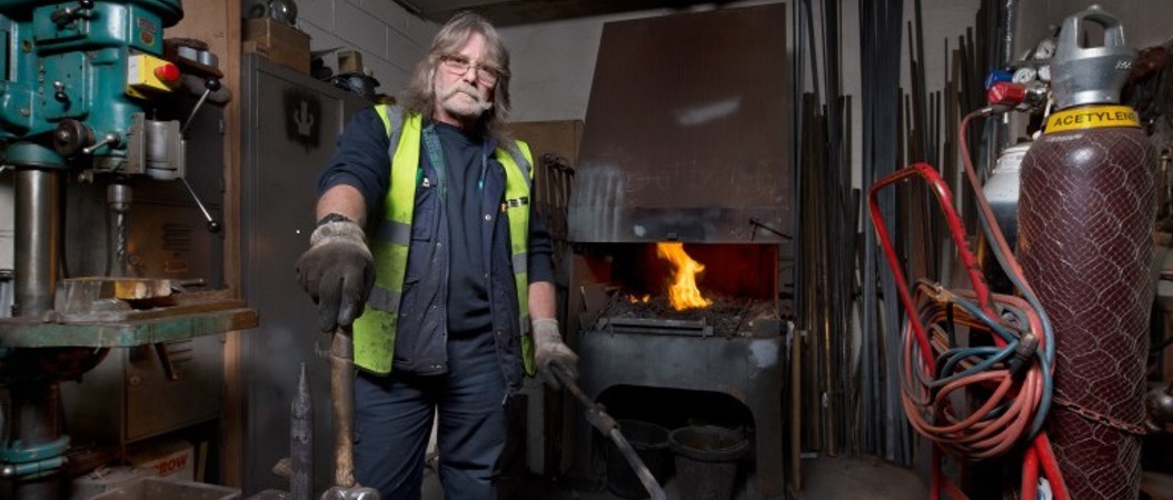 A blacksmith in a workshop standing beside an anvil