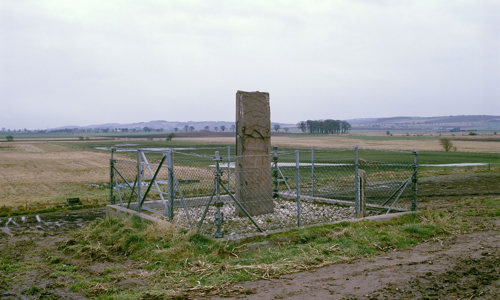  A tall Pictish cross-slab with a prominent, ornate cross carved on the front. Detail shows a hunting scene and a boat.