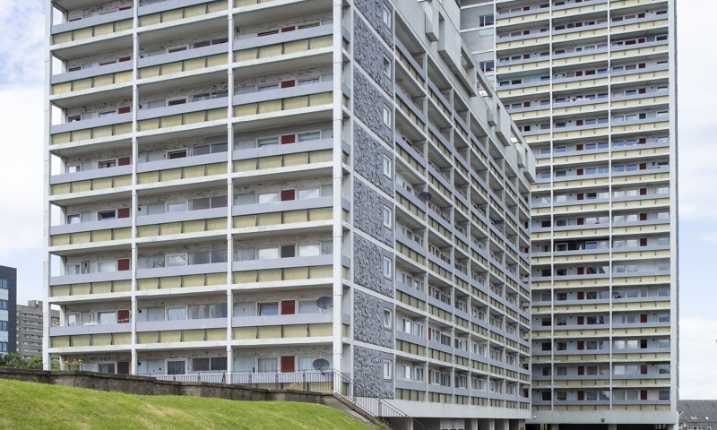 A high rise block of flats with cars parked outside 