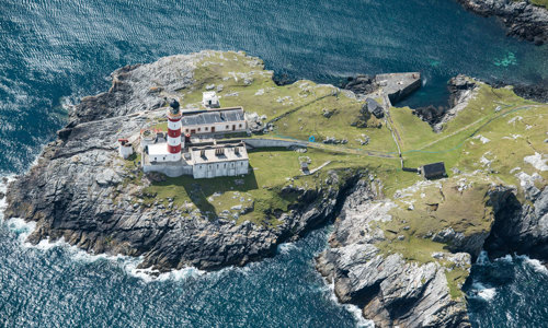 A red and white lighthouse perched on cliffs about the sea. 