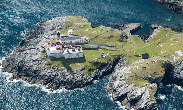 A red and white lighthouse perched on cliffs about the sea. 