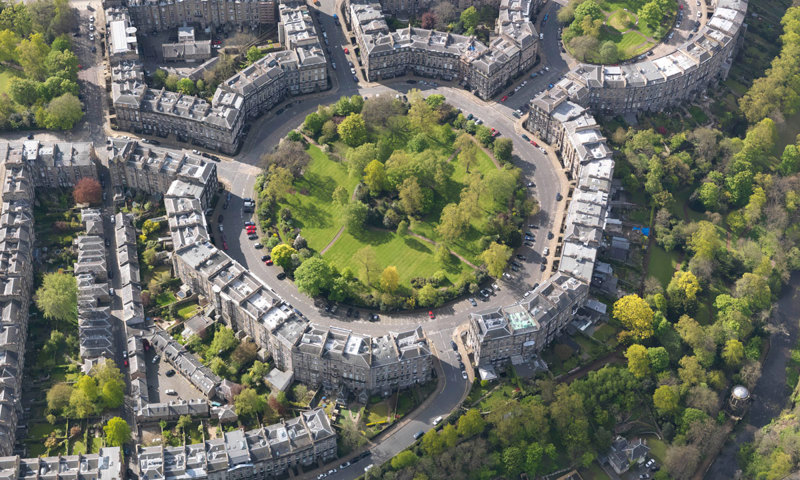 A green space roundabout surrounded by tenement buildings and trees.