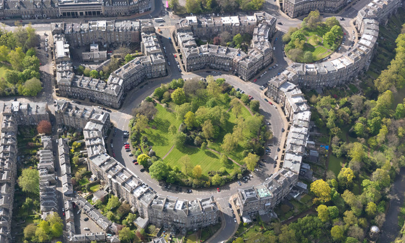 A green space roundabout surrounded by tenement buildings and trees.